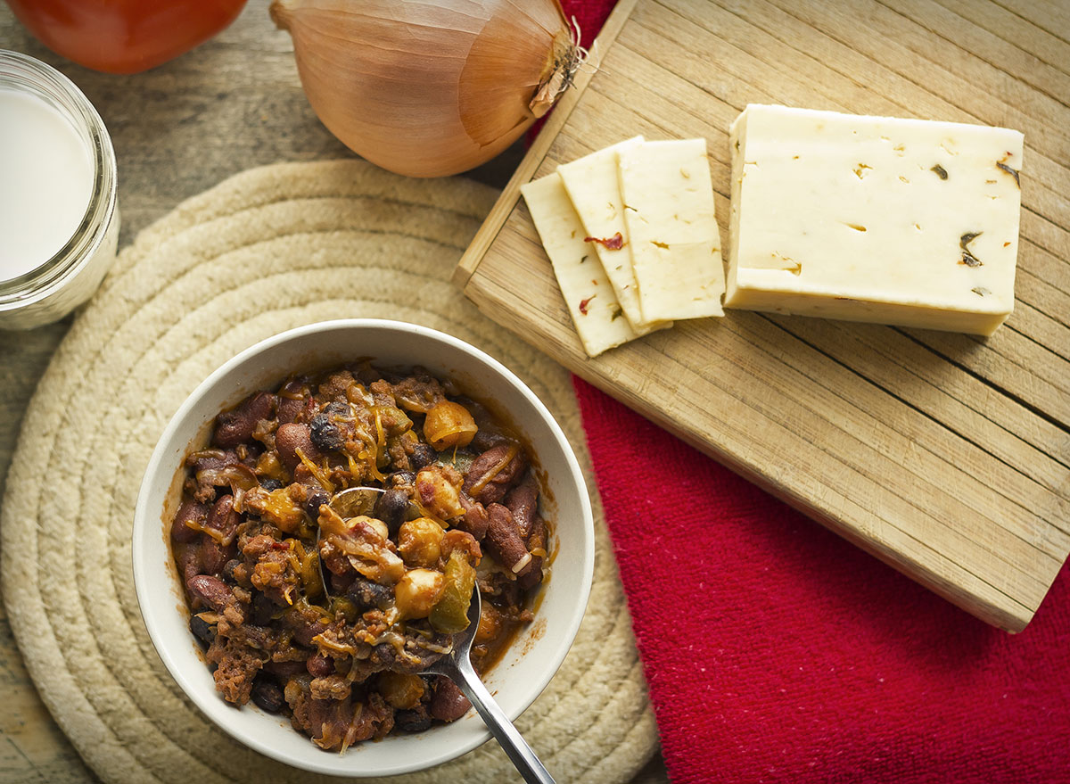 Slices of pepper jack cheese on a cutting board with a bowl of chili