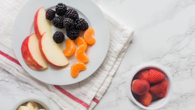 Plate of fruit - apple slices tangerines blackberries - and bowls of strawberries bananas