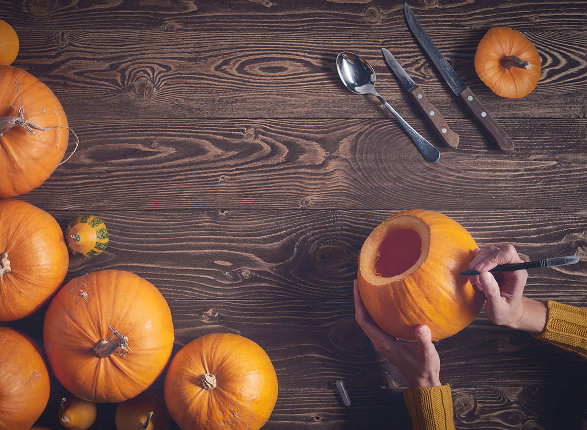 hands drawing pumpkin carving template with group of pumpkins