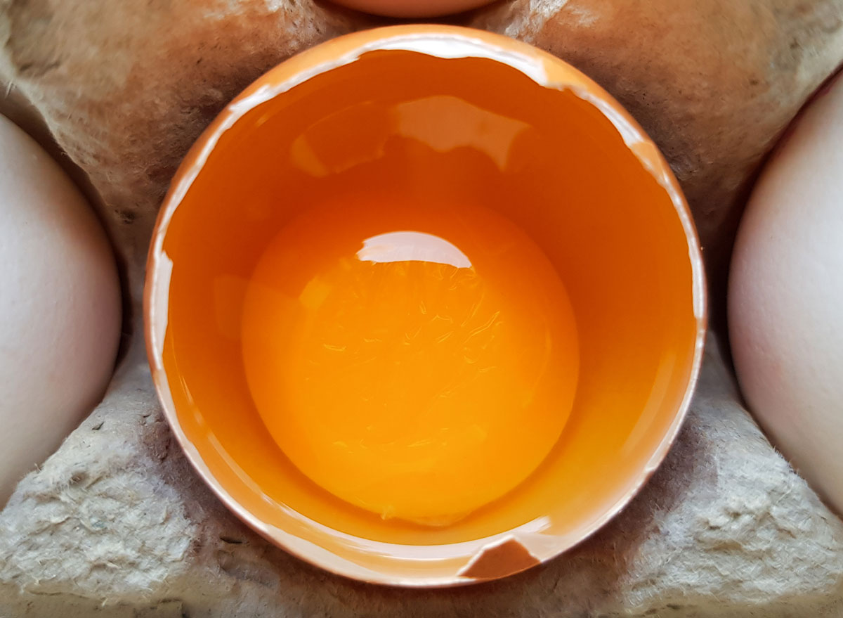 Raw egg yolk in cracked shell in egg carton