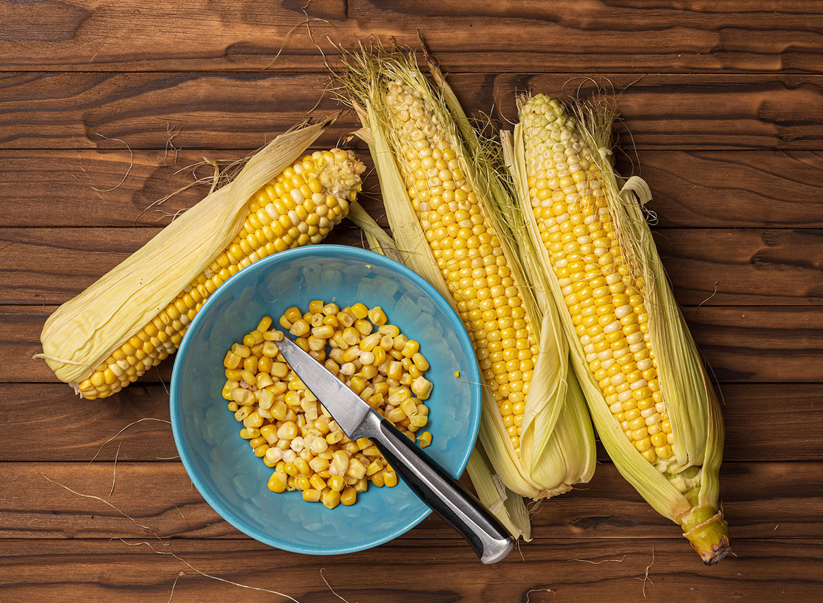 Shucking corn with a knife in a bowl