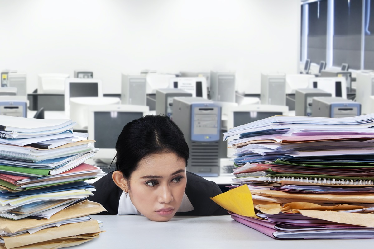 Overworked businesswoman with many jobs, looking at pile of documents with bored expression