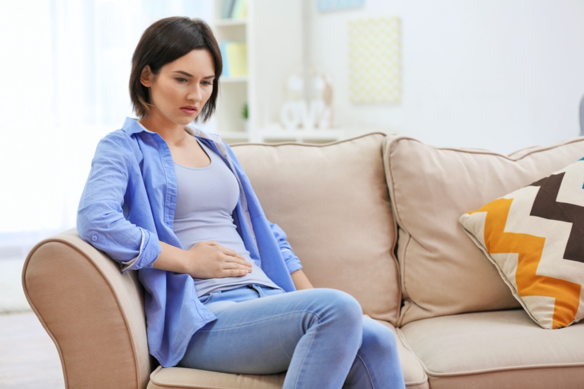 woman suffering from abdominal pain while sitting on sofa