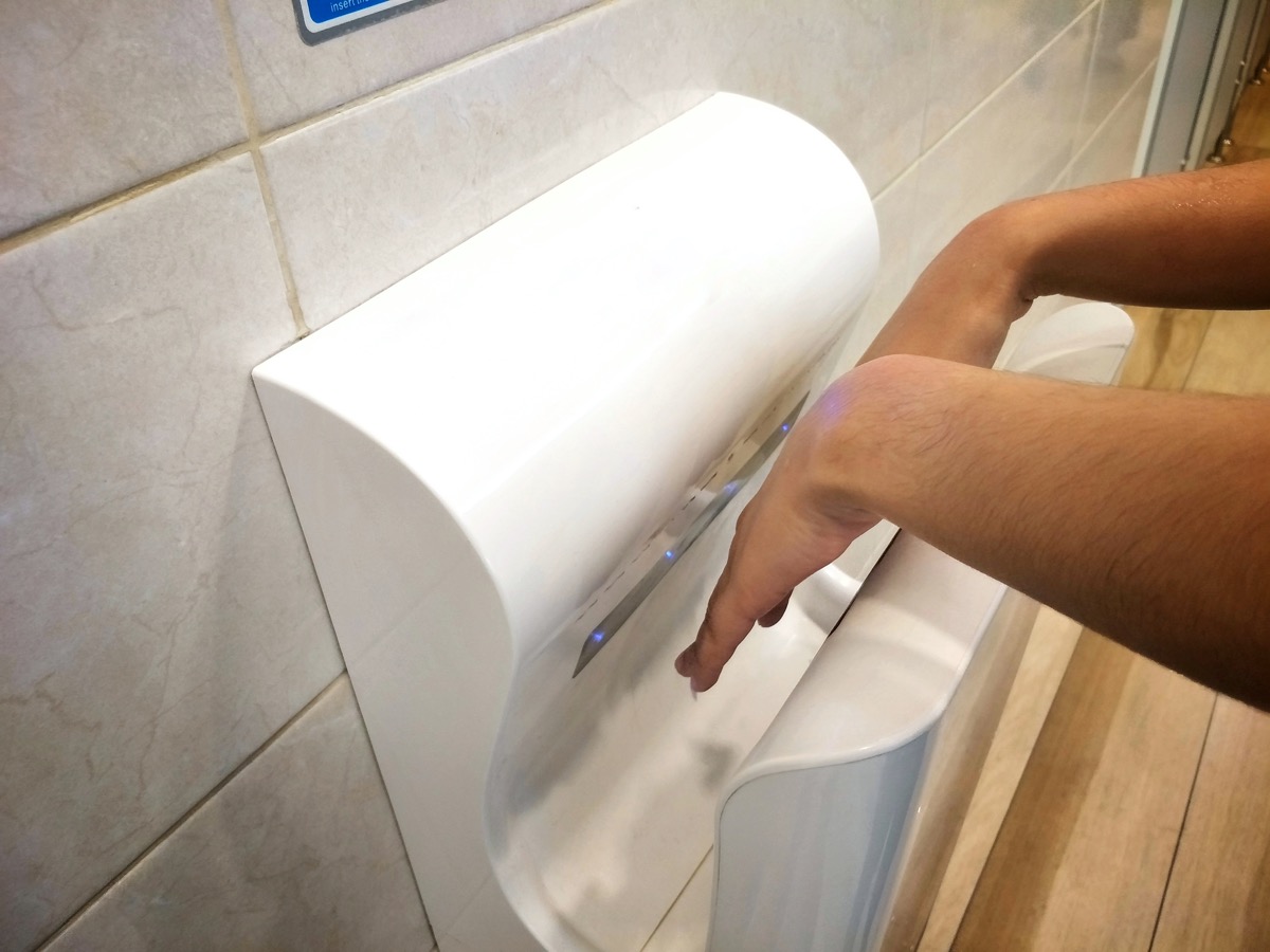 Female dries wet hand in modern vertical hand dryer in public restroom