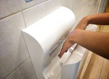 Female dries wet hand in modern vertical hand dryer in public restroom