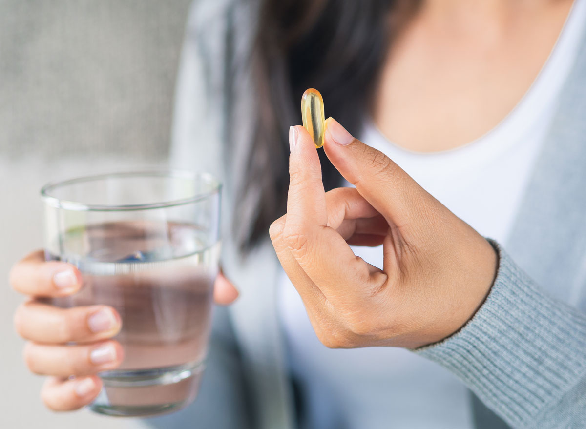 Woman holding fish oil vitamin pill supplement alongside a glass of water