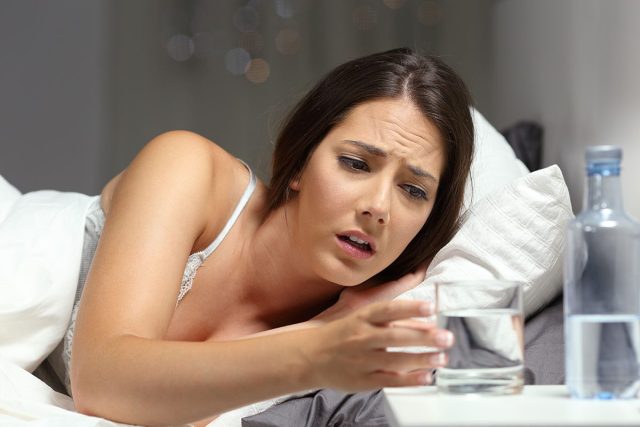 A woman in bed, feeling thirsty, touches the water