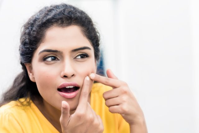 woman looking in mirror squeezing pimple