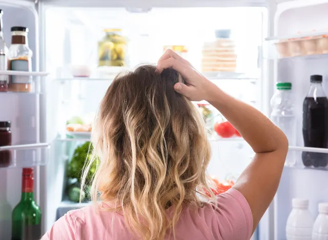 Woman standing at refrigerator hungry and confused