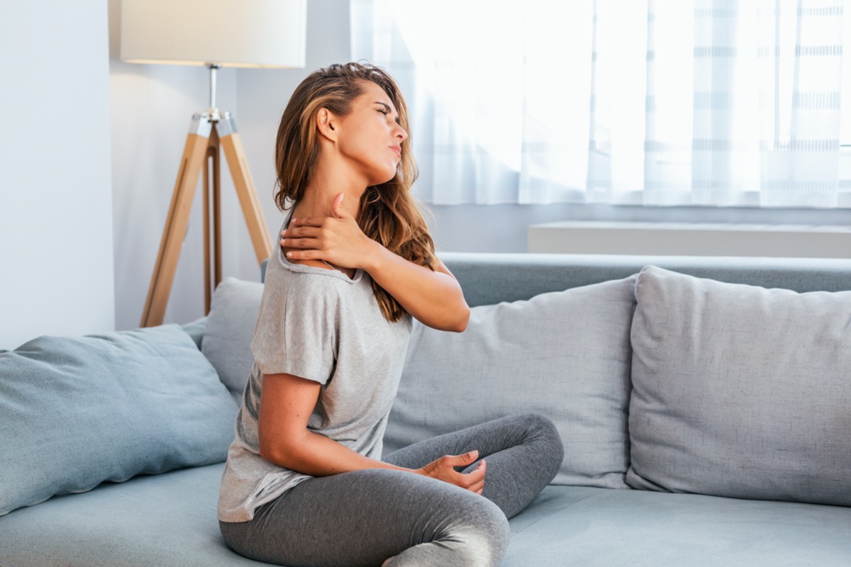 woman sitting on the bed and holding painful shoulder with another hand