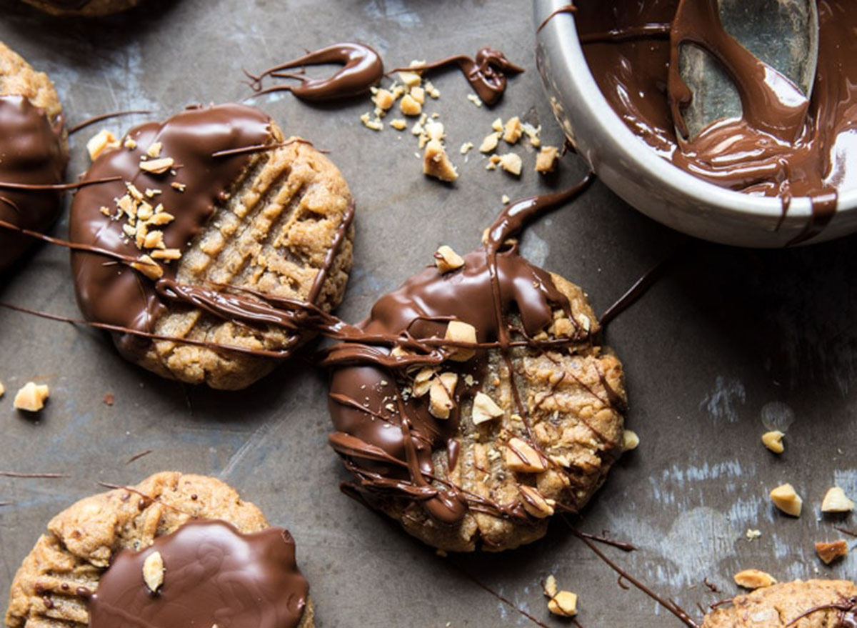 Chocolate dipped peanut butter cookies with nuts on a dark counter