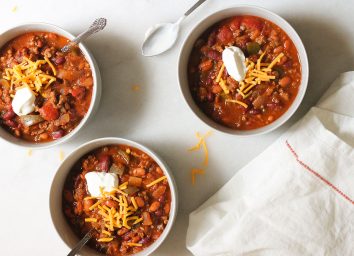 wendy's copycat chili in three bowls on a marble counter with cheese and sour cream