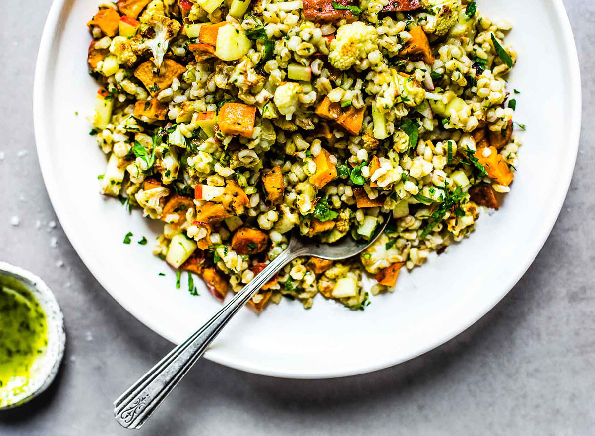 autumn glow salad with grains apples sweet potato and pesto in white bowl with spoon