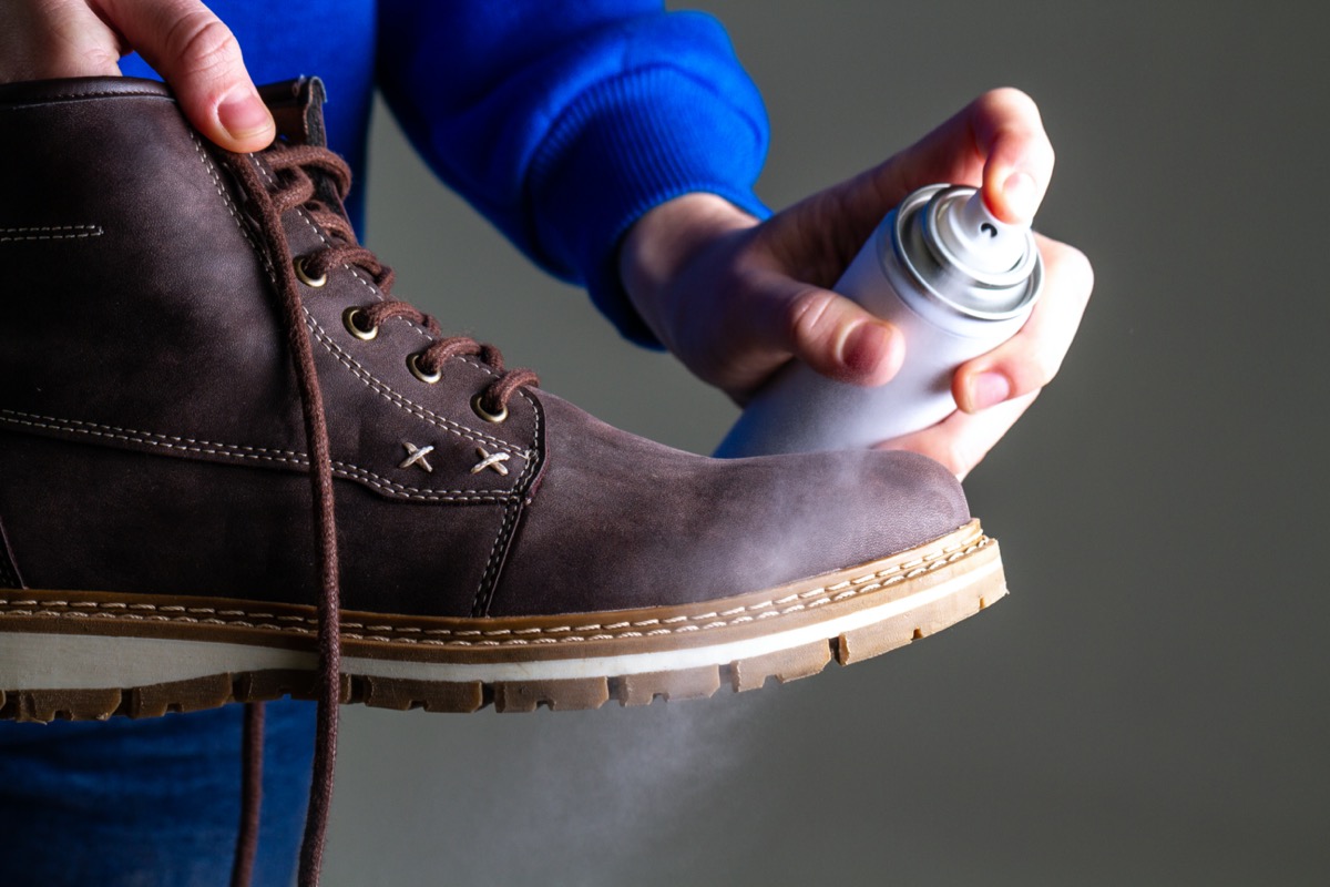 A person is cleaning and spraying agent on men's suede casual boots for protection from moisture and dirt