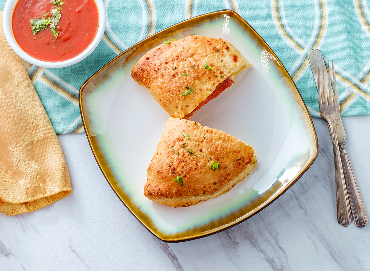 calzone cut in half on a plate with a bowl of marinara sauce