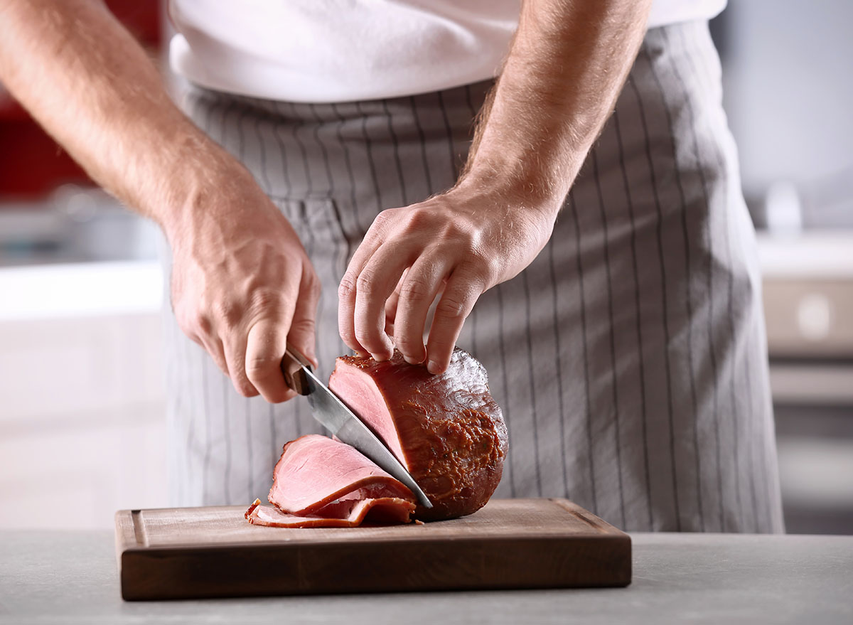 chef slicing ham on wooden block