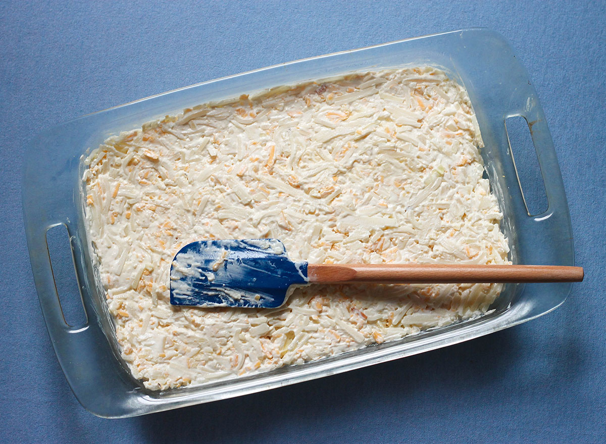 Pouring hashbrown casserole ingredients into a casserole dish