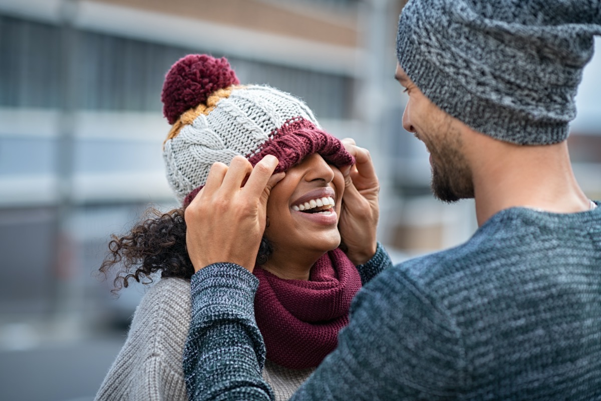 couple having fun outdoor in winter. Young man covering eyes his girl with woolen cap