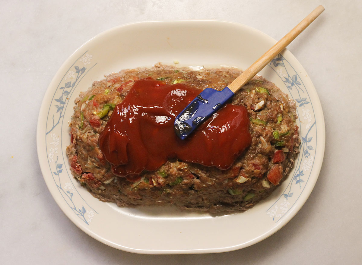 Spreading ketchup on the cooked meatloaf.