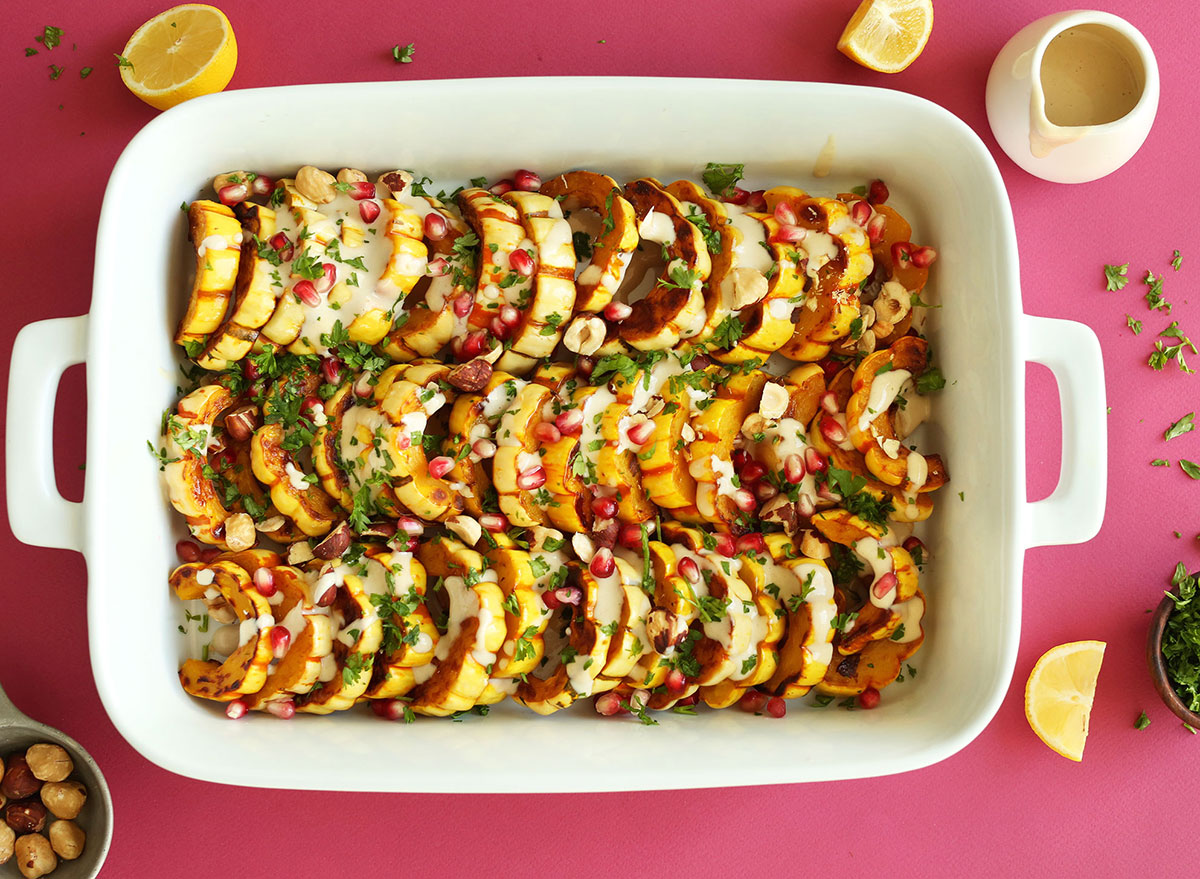 sliced delicata squash with pomegranate seeds and garnish in white baking dish