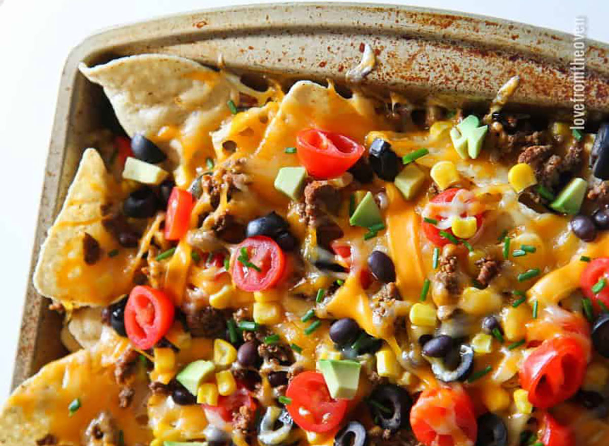 easy nachos with cheese tomatoes avocado olives on baking sheet