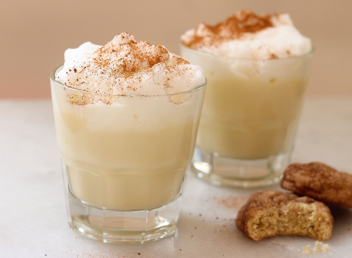 two cups of eggnog sprinkled with nutmeg next to two cookies