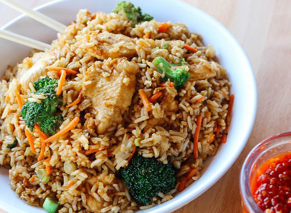 bowl of fried rice with chicken and vegetables and a side of hot spicy sauce
