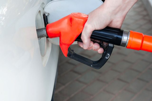 A man's hand holds a filling gun inserted into the hole of a gasoline tank of a car on a gasoline fueling