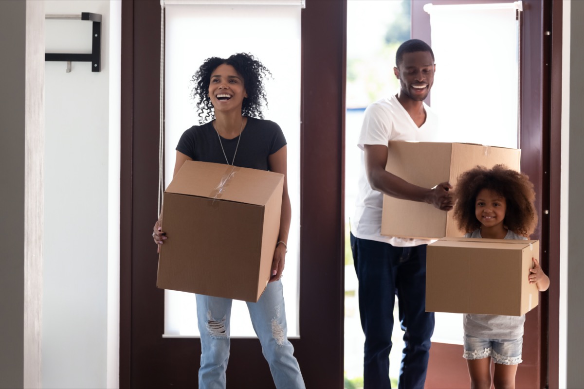 Family with kid girl entering big modern house holding boxes on moving day, happy parents and child daughter standing in hallway looking around, tenants