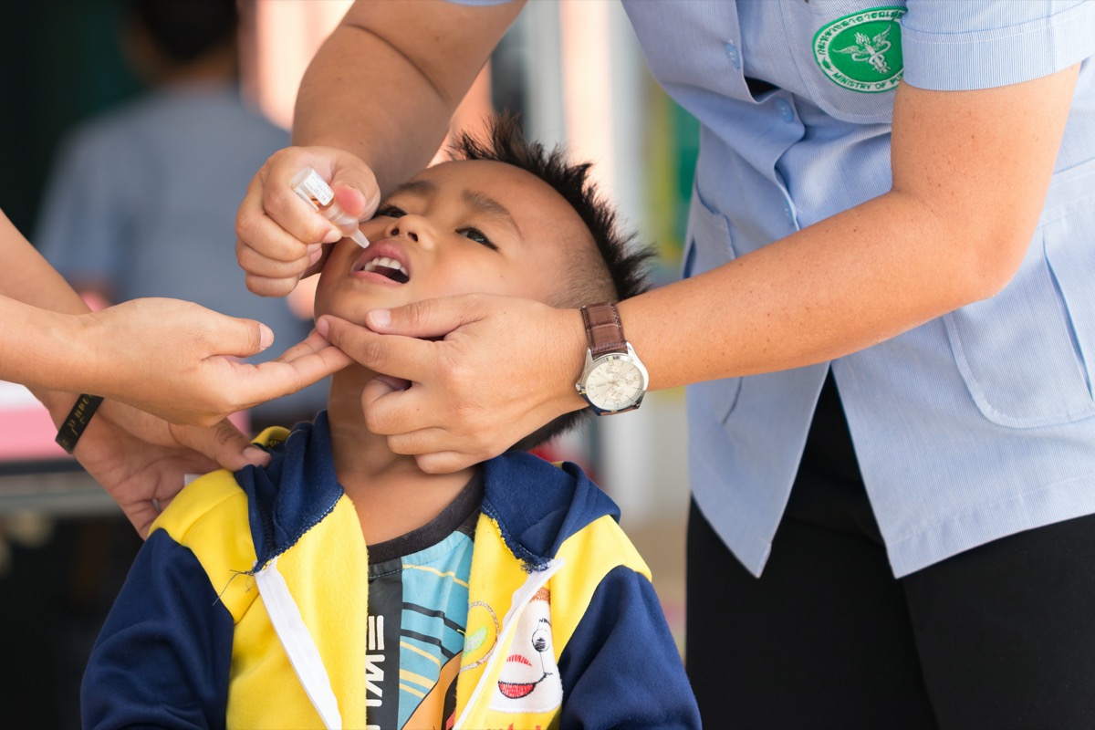 Health worker drops oral polio vaccine into child's mouth for prevention of poliomyelitis