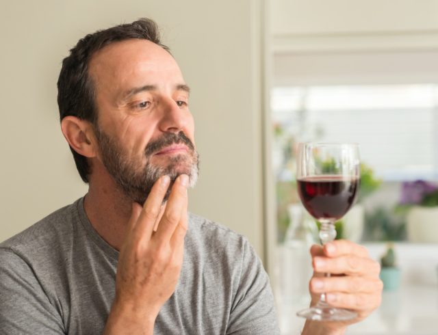 Middle age man drinking a glass of wine serious face thinking about question, very confused idea