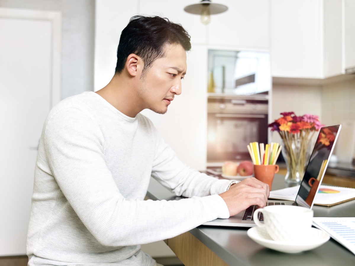 man working from home sitting at kitchen counter using laptop computer