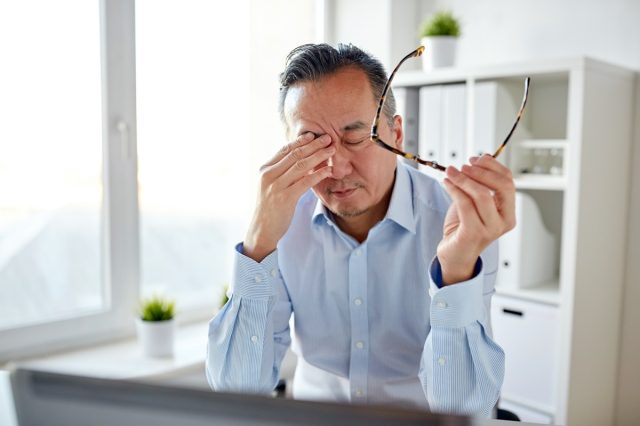 tired businessman with eyeglasses and laptop computer rubbing eyes at office