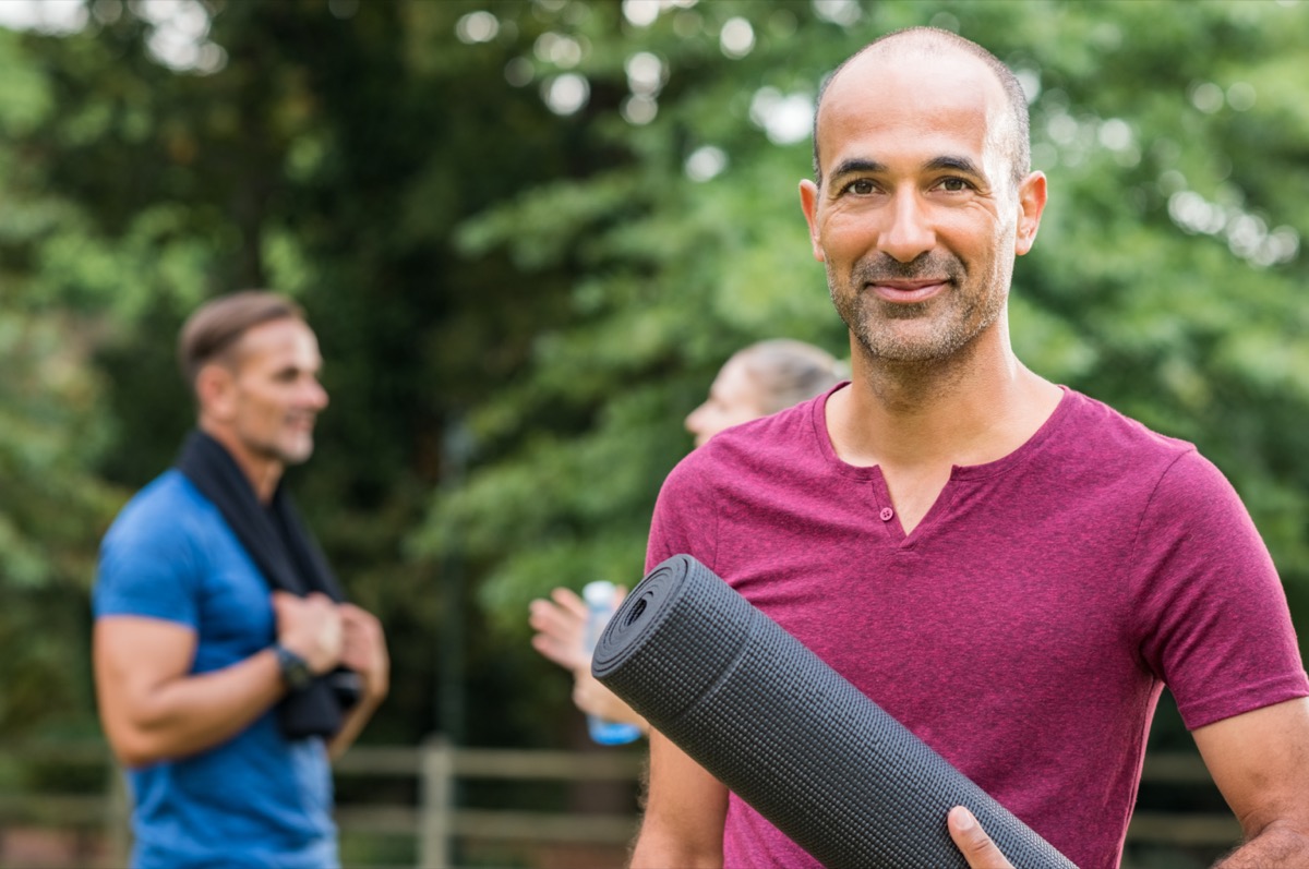 mature man holding yoga mat and looking at camera