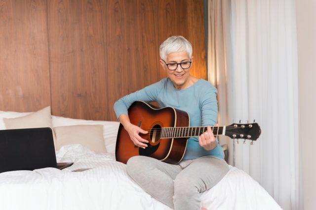 Zralá žena hrající na kytaru ve své ložnici, volný čas a koníčky