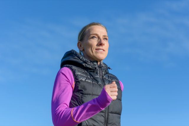 mulher de meia idade correndo no inverno em uma visão de baixo ângulo de perto contra um céu azul ensolarado em um estilo de vida ativo e saudável