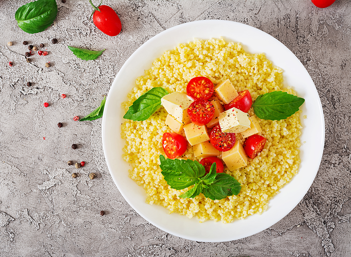 bowl of millet porridge with basil leaves cheese cubes and cherry tomato halves