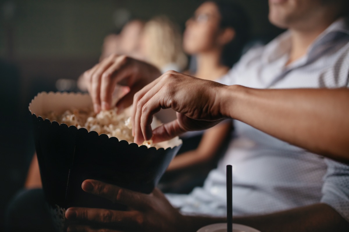 people eating popcorn in movie theater, focus on hands