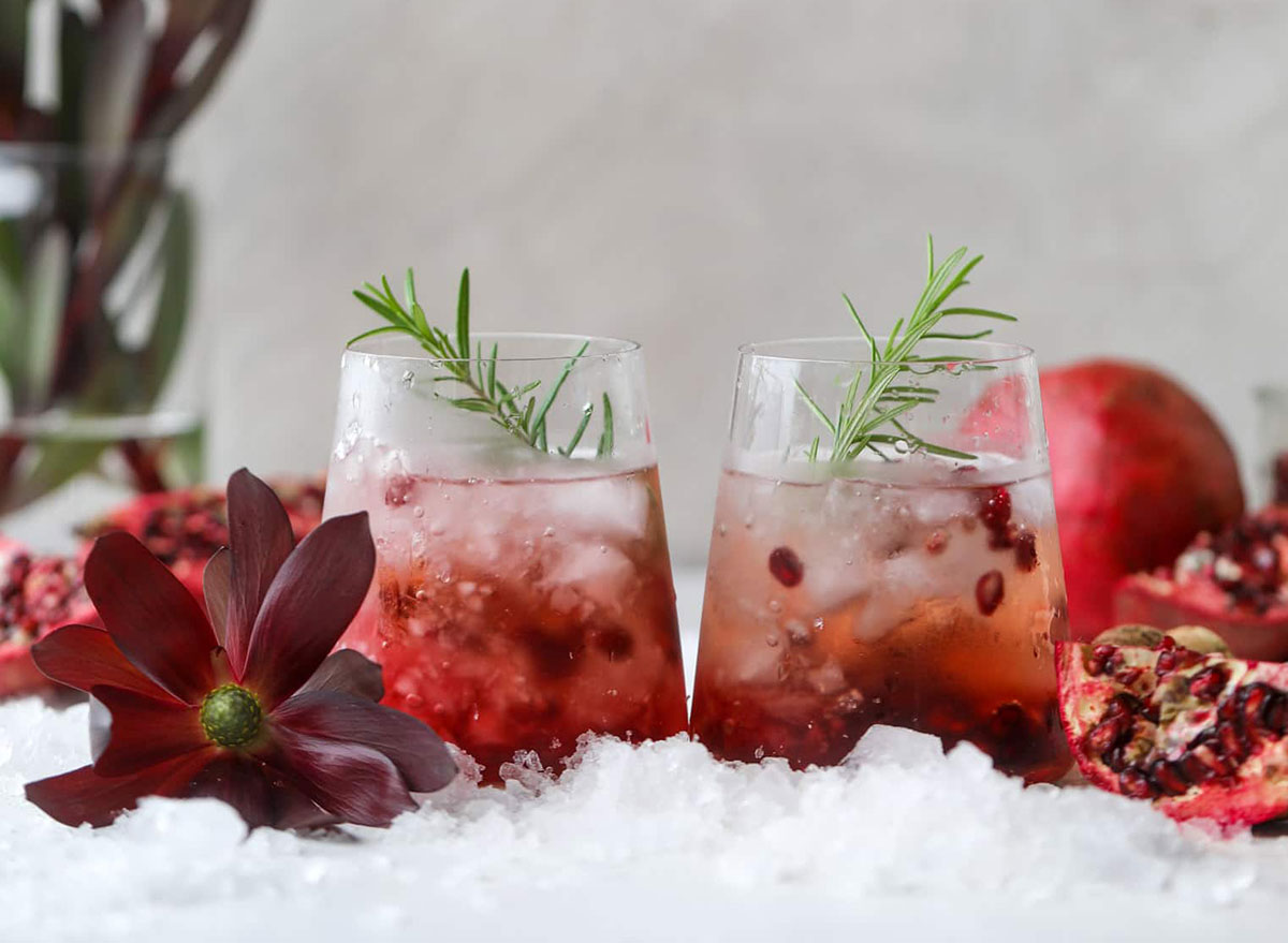 two glasses of pomegranate prosecco cocktail with flowers and ice and pomegranate slices