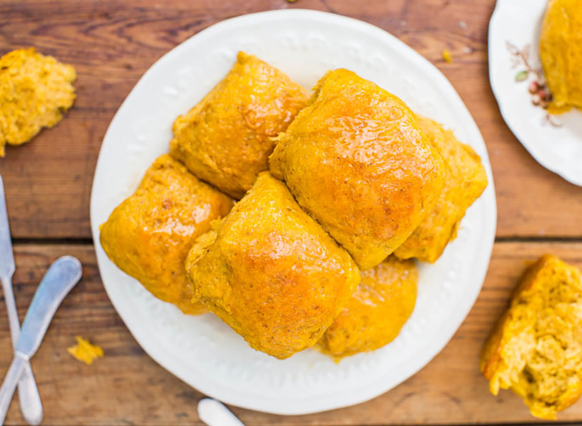 pumpkin dinner rolls with honey butter on white plate on wooden table