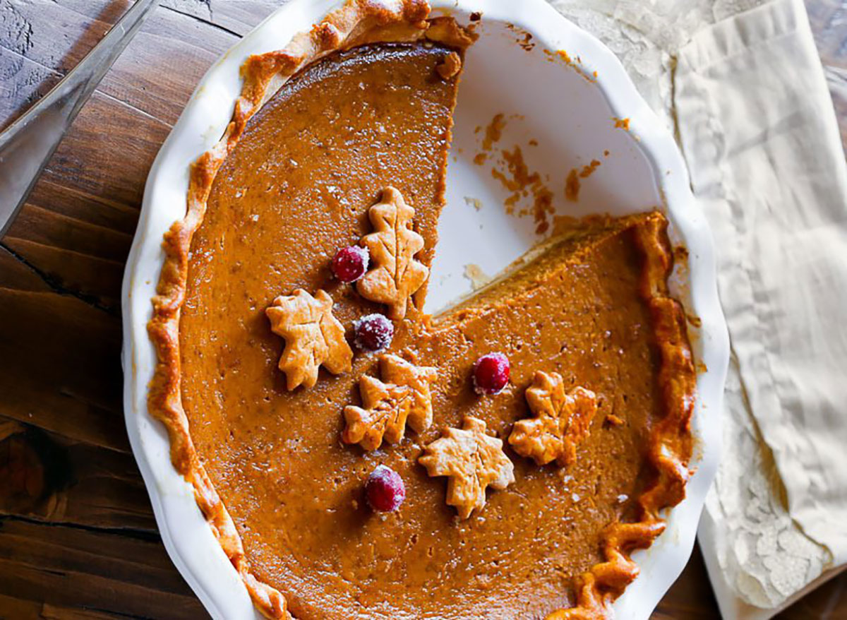 pumpkin pie in white baking dish topped with leaf cutouts and cranberries