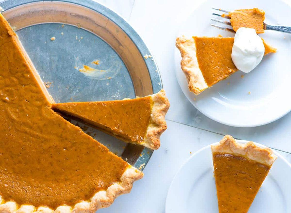 pumpkin pie in metal baking dish with two slices on white dessert plates