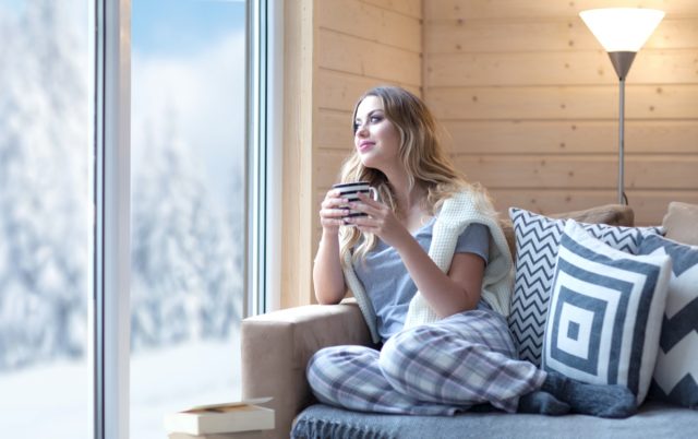 woman with a cup of coffee sitting at home in the living room near the window.  Winter snow landscape view