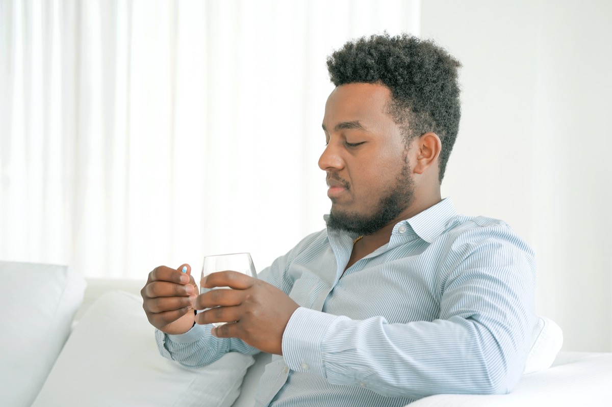 man holding pill glass of water at home on the sofa