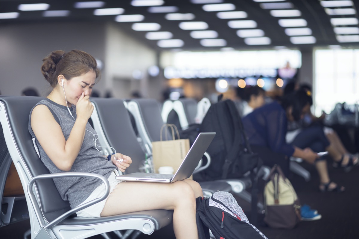 woman got nose allergy, flu sneezing nose sitting at the chair in airport with laptop computer in her lap