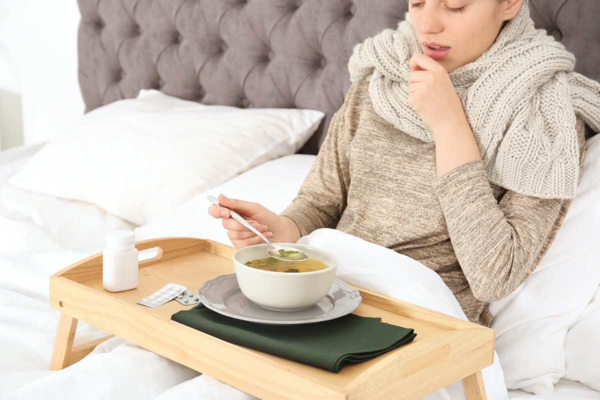 Sick young woman eating broth to cure cold in bed at home
