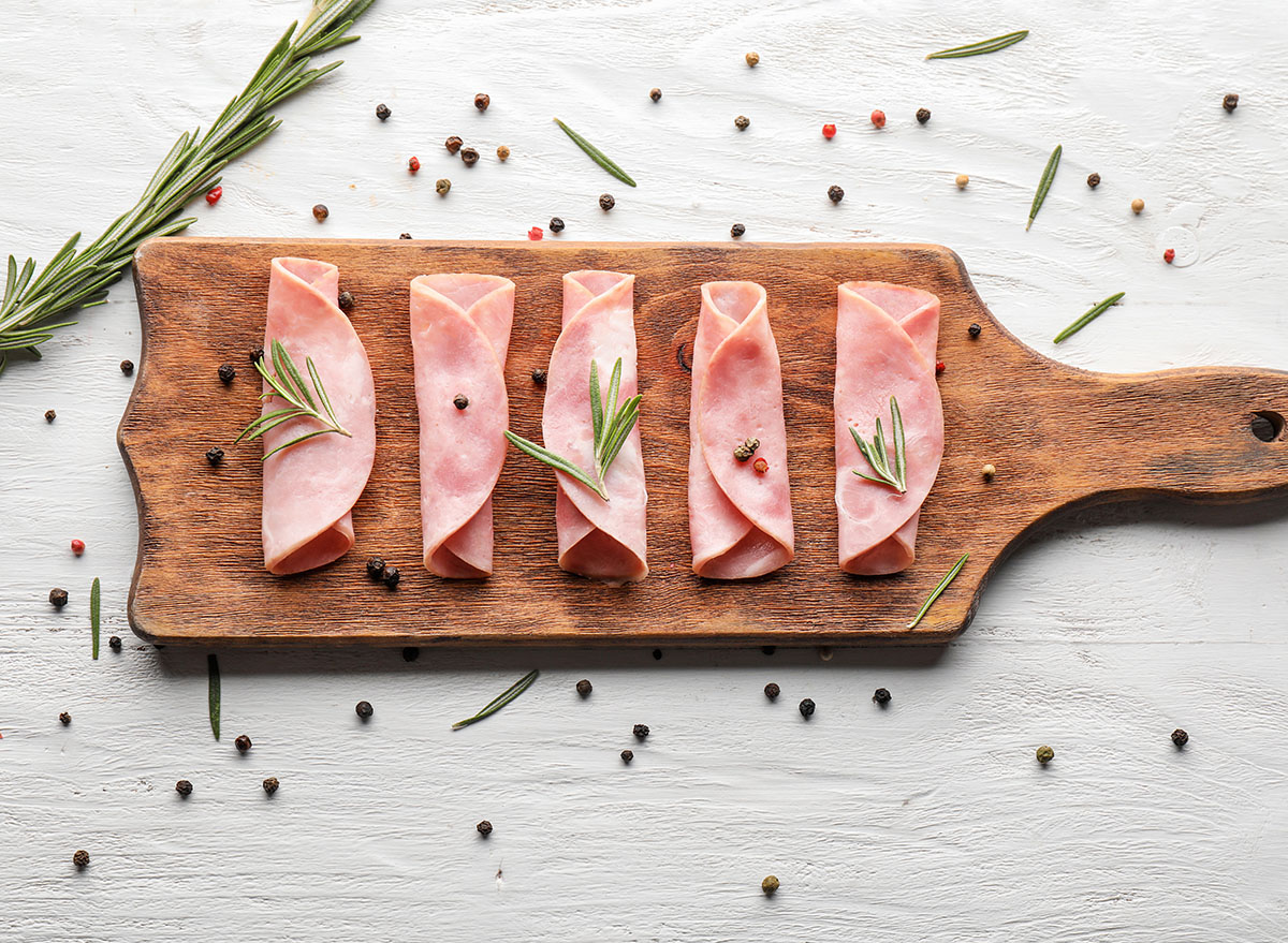 sliced ham on wooden board with rosemary and pepper garnish