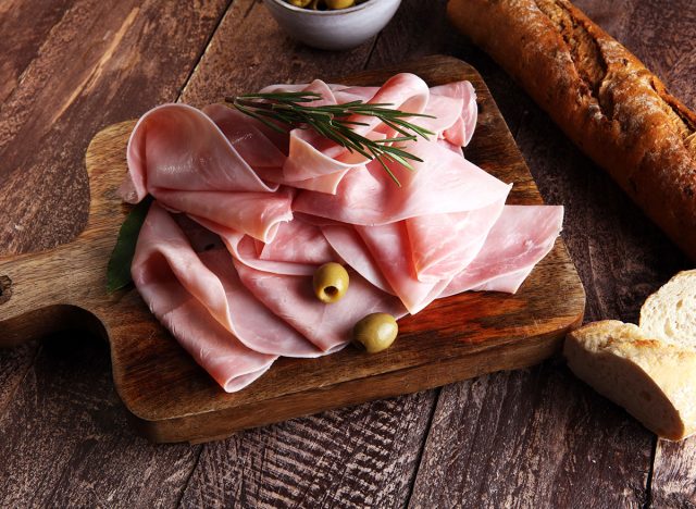 sliced ham on wooden cutting board and rosemary and olive garnish