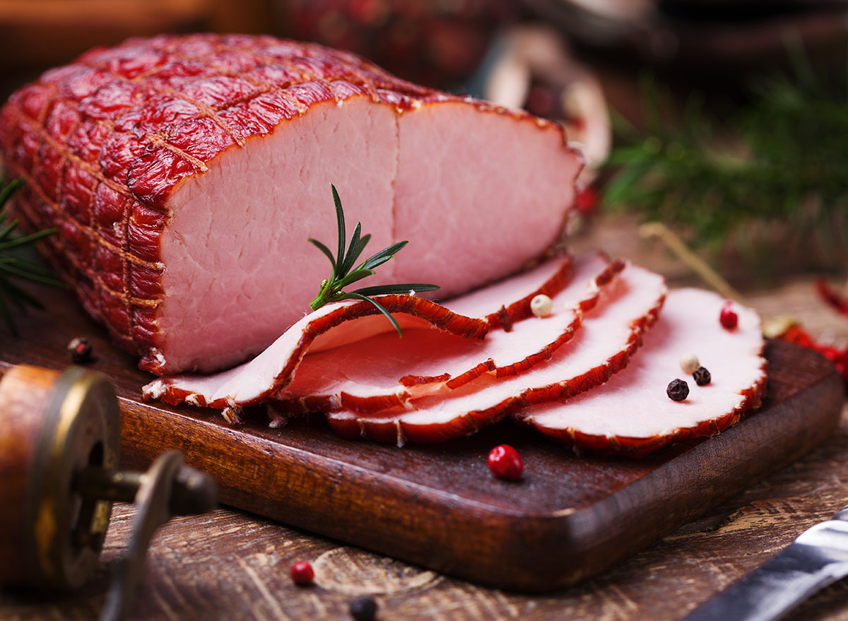 smoked ham on wooden cutting board with peppercorns and rosemary