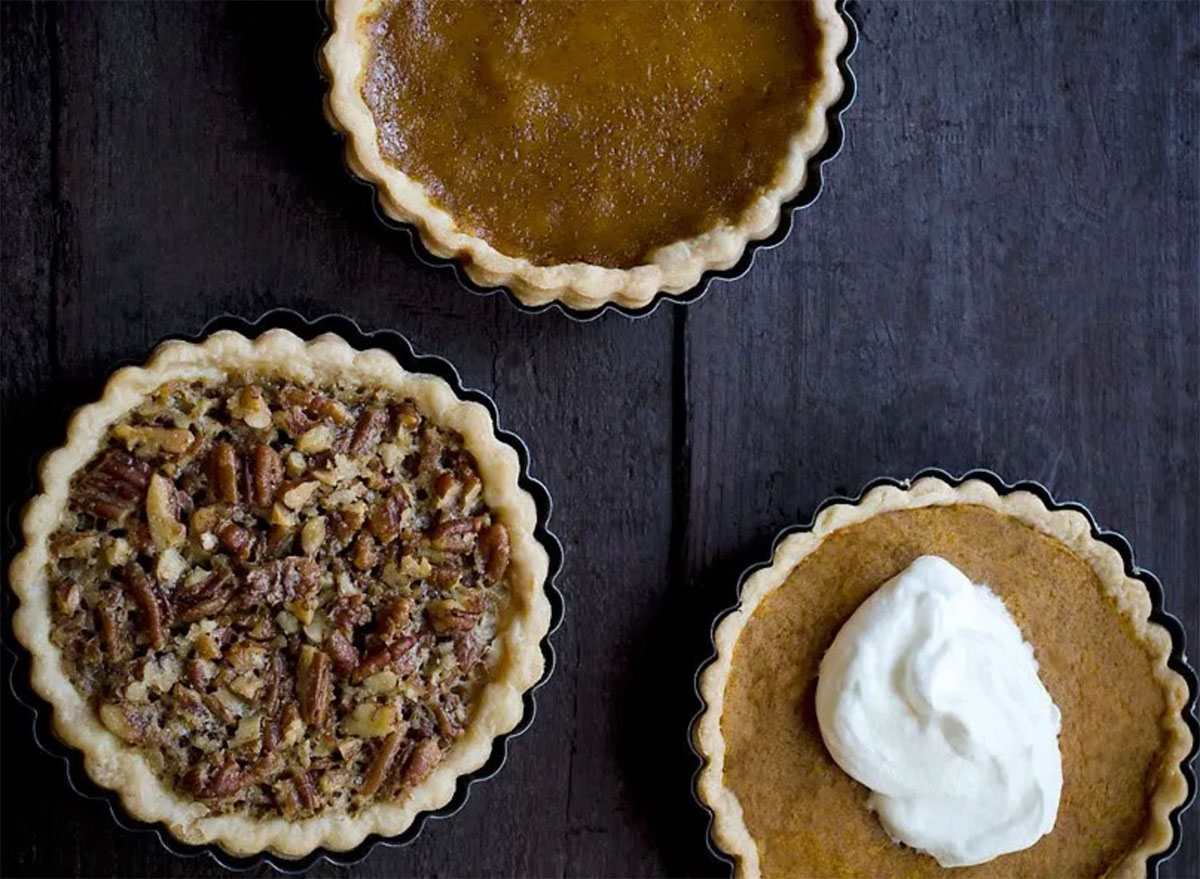 three thanksgiving pie tarts pecan and pumpkin in baking dishes on wood table